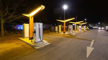 Illuminated electric vehicle charging stations lined up in a parking area at night.