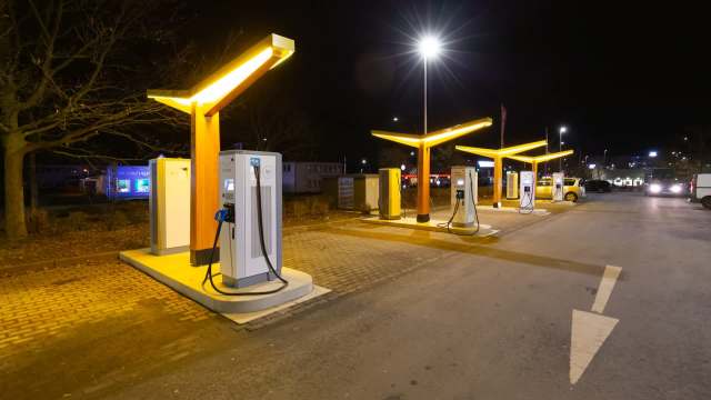 Illuminated electric vehicle charging stations lined up in a parking area at night.
