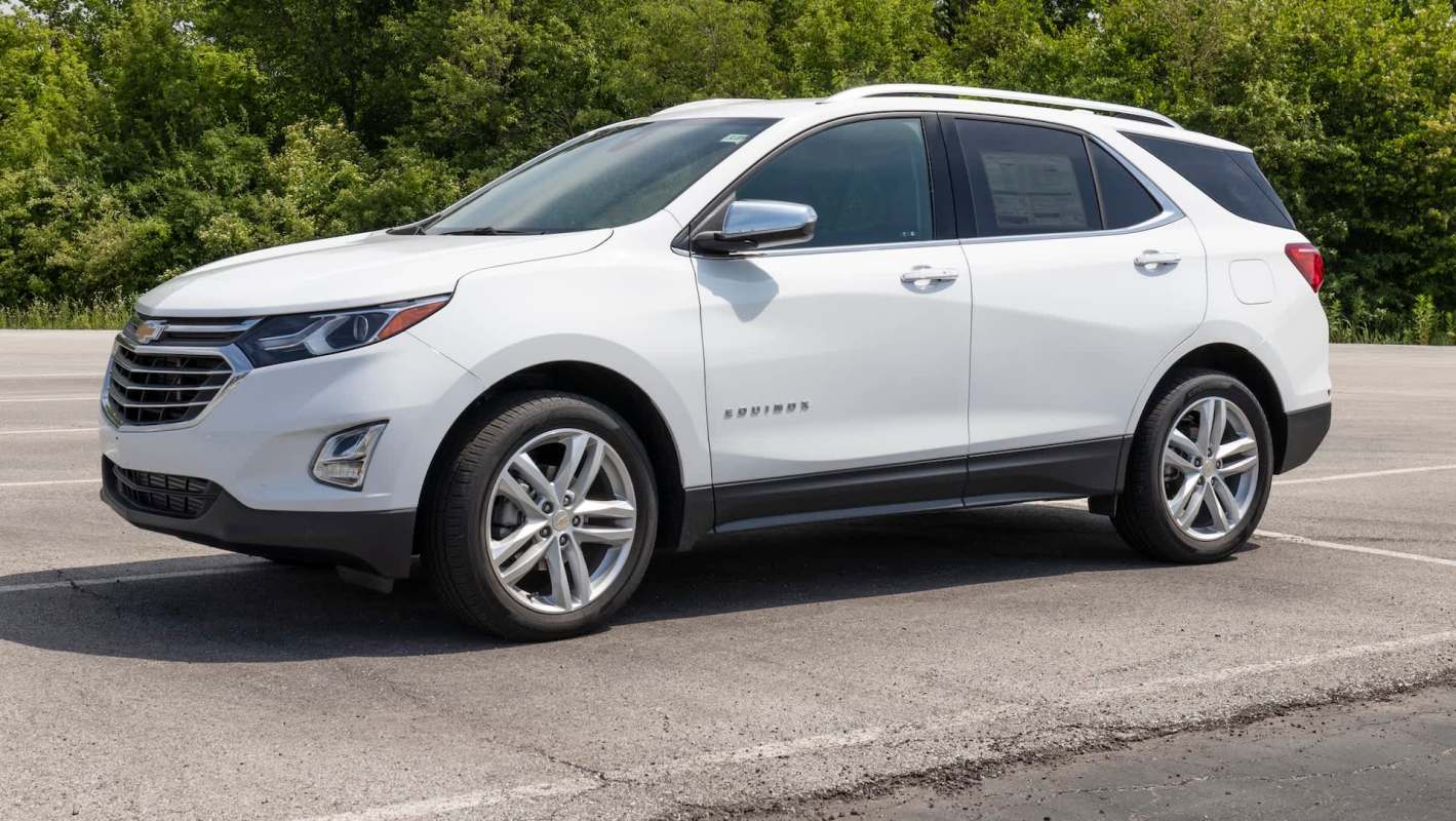 A white Chevrolet Equinox parked on an asphalt lot with greenery in the background.