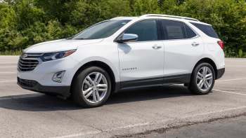 A white Chevrolet Equinox parked on an asphalt lot with greenery in the background.