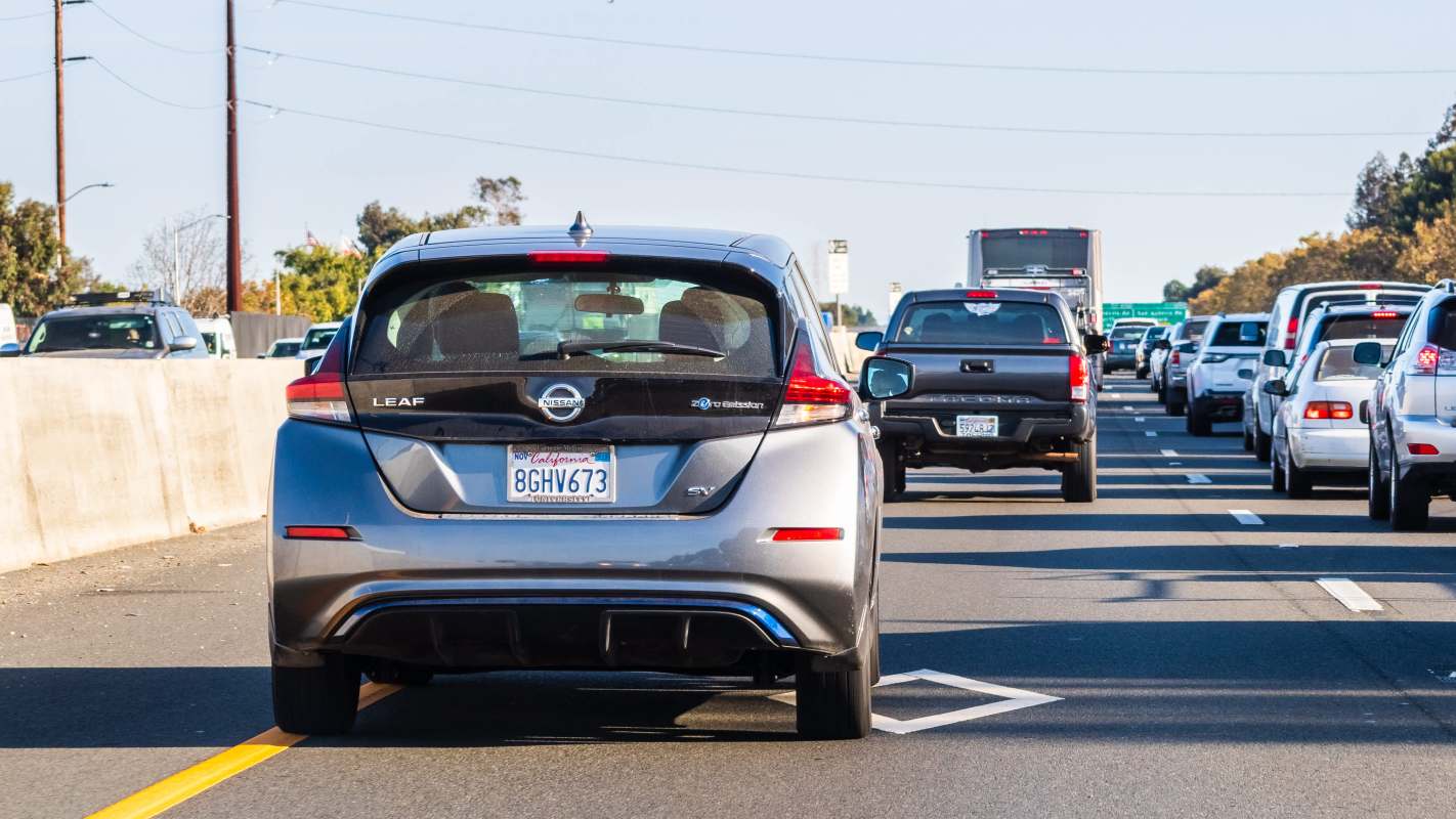 A gray Nissan Leaf is in the foreground of heavy traffic on a highway.