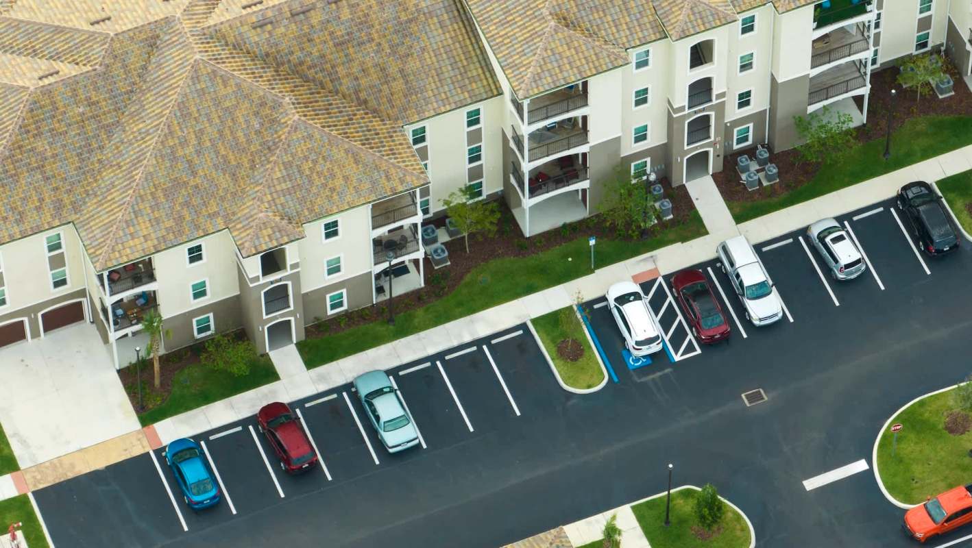 Aerial view of an apartment complex with parked cars in front and balconies visible on the second floor.