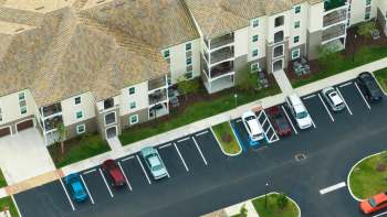 Aerial view of an apartment complex with parked cars in front and balconies visible on the second floor.