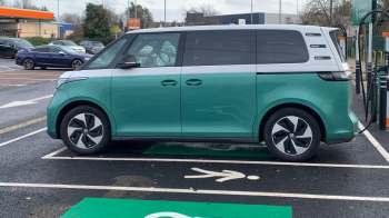 A green and silver electric van parked in a charging station with a pedestrian symbol on the ground.