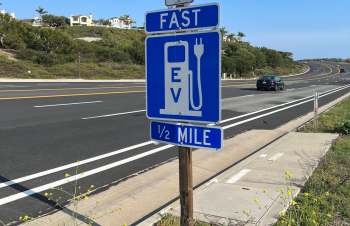 A sign indicating a fast EV charging station is ½ mile ahead, next to a highway.