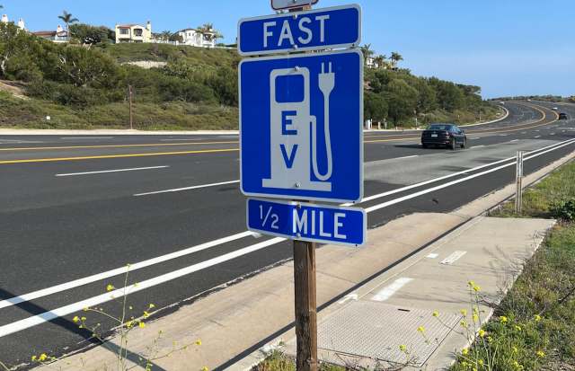A sign indicating a fast EV charging station is ½ mile ahead, next to a highway.