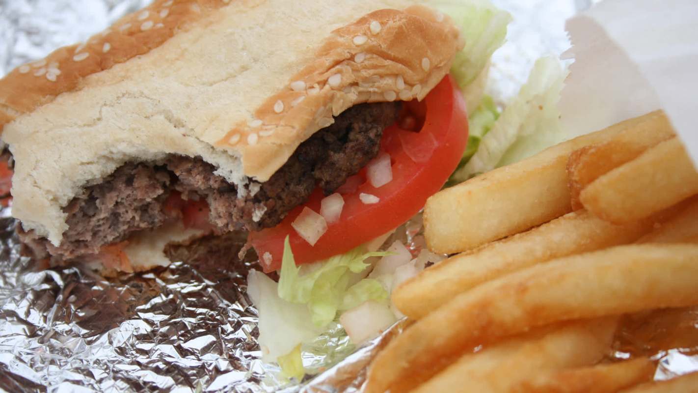 A close-up of a sesame seed hamburger with lettuce, tomato, and onion beside a serving of French fries.