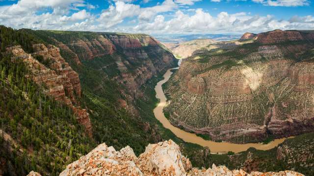 A sweeping view of a river winding through rugged cliffs and green forests under a partly cloudy sky.