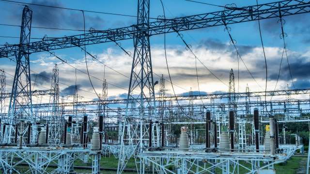 An electric substation featuring various towers, wires, and equipment against a blue sky and clouds.