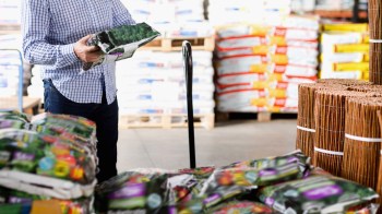 A person examines a bag of soil in a warehouse filled with gardening supplies.
