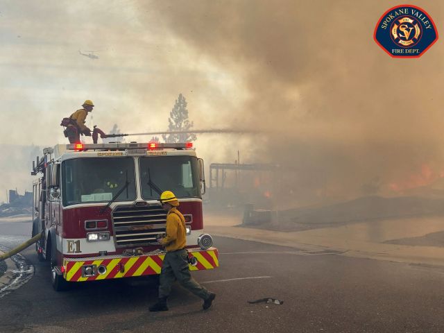A firefighter on a firetruck spraying a fire.