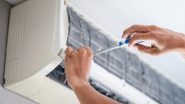 A person using a screwdriver to repair or maintain an air conditioning unit.