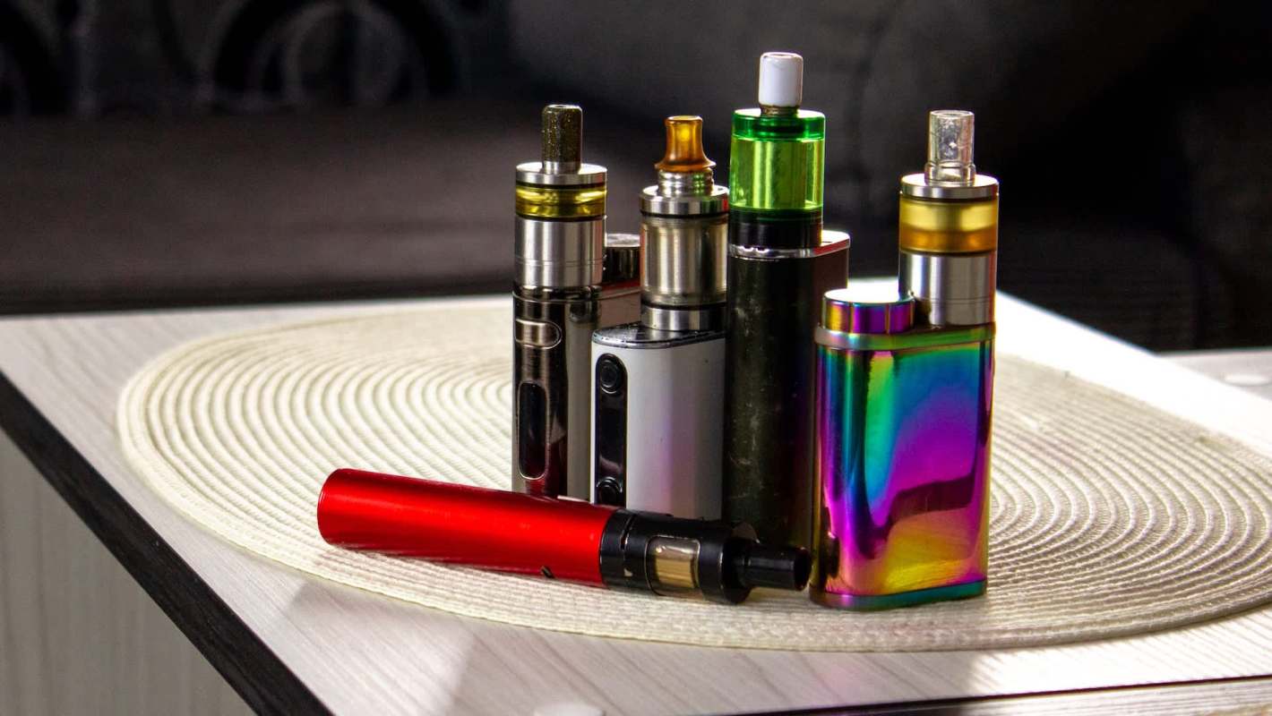 A variety of colorful vape devices arranged on a circular tabletop placemat.