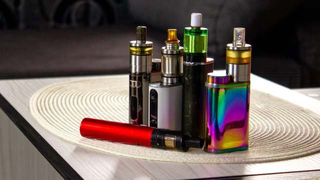 A variety of colorful vape devices arranged on a circular tabletop placemat.