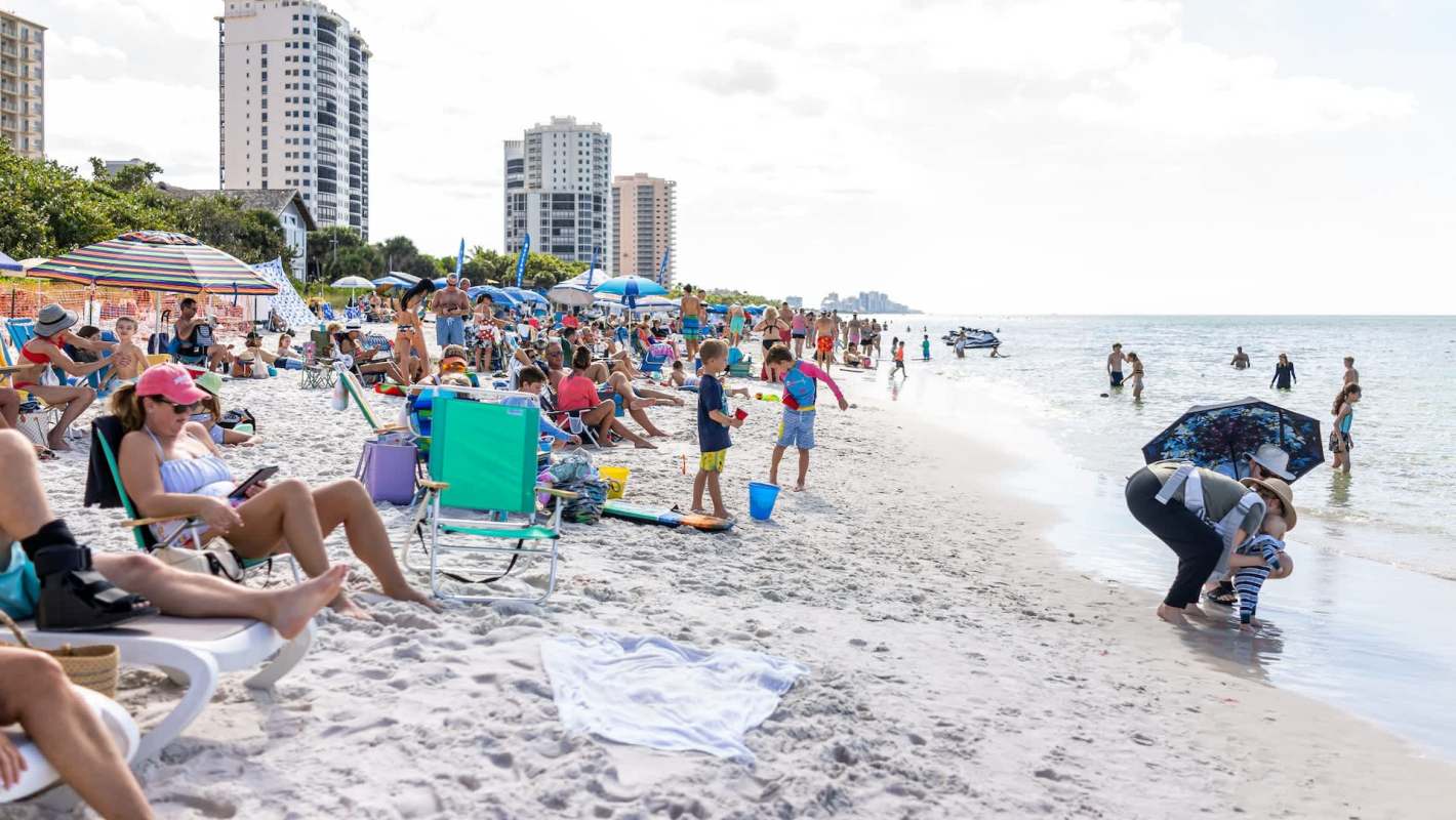 A crowded beach with families lounging under umbrellas and children playing.