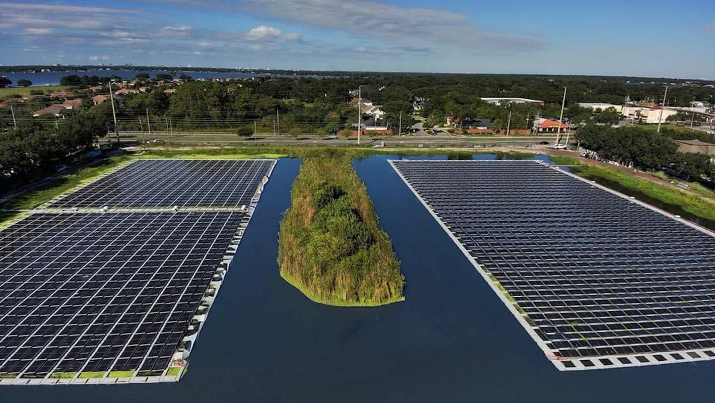 Aerial view of solar panels installed on a lake with a small island of vegetation in the center.