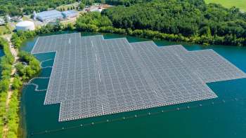 Aerial view of a large floating solar panel installation on a body of water surrounded by greenery and buildings.