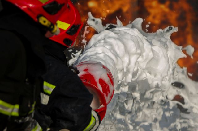 A firefighter sprays foam from a nozzle.