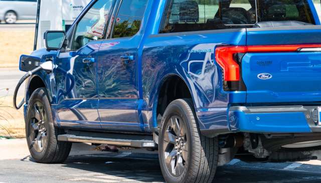 A blue Ford F-150 Lightning electric truck charging at a station.