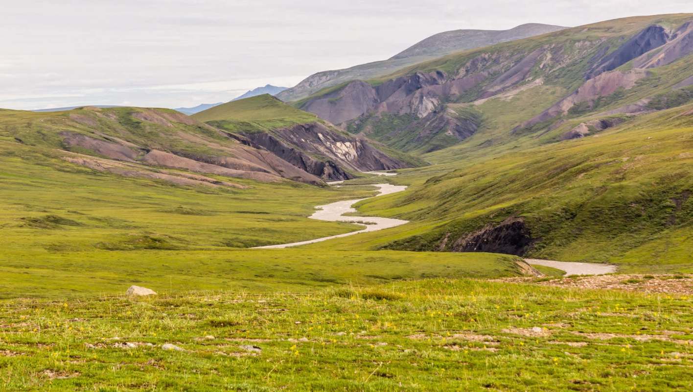 A winding river flows through a lush green valley surrounded by rugged mountains under a cloudy sky.