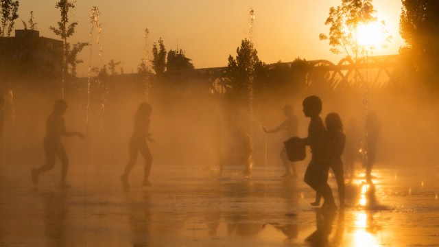 Children play and splash in a fountain at sunset.