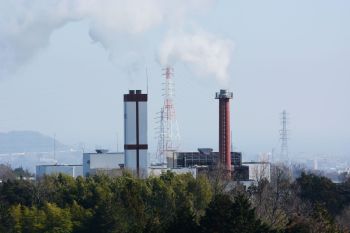 Industrial smokestacks emit white smoke.