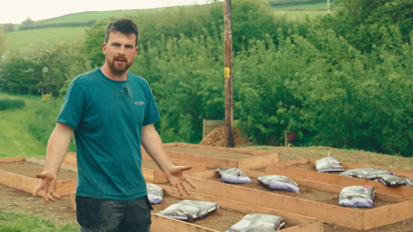 A man in front of wooden raised garden beds and soil bags.