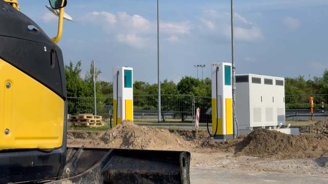 A construction site featuring two electric vehicle charging stations beside a bulldozer and mounds of dirt.