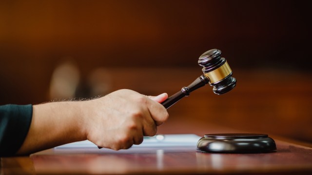 A close-up of a hand holding a gavel above a sound block in a courtroom setting.