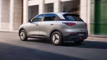 A silver EX2 electric hatchback drives past urban buildings.