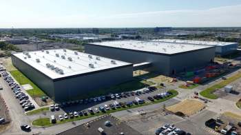 Aerial view of a large industrial building surrounded by parked cars and construction.