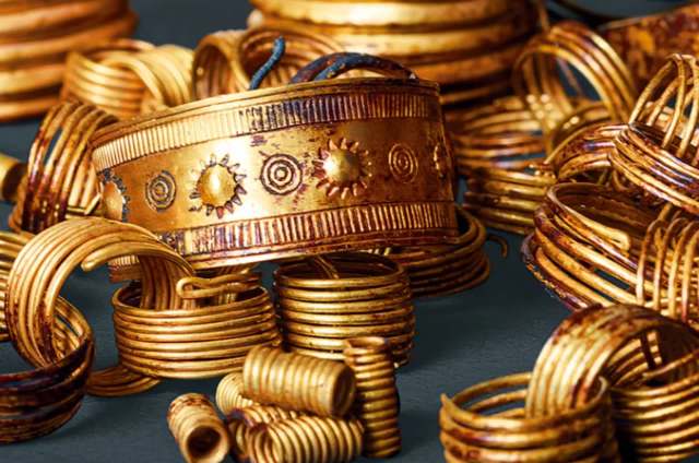 A collection of intricate golden jewelry pieces, including decorative bracelets and coils, scattered on a surface.