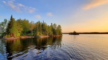 A serene view of a lake bordered by lush green trees under a colorful sunset sky.