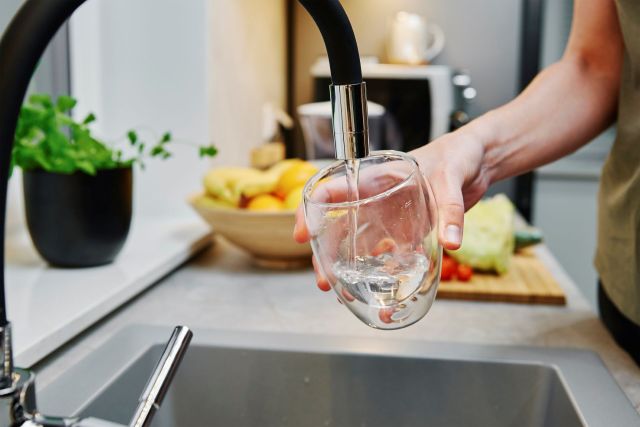A person filling a glass with water from a kitchen faucet.