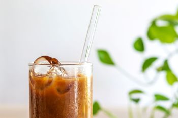 A glass of iced coffee with a glass straw.