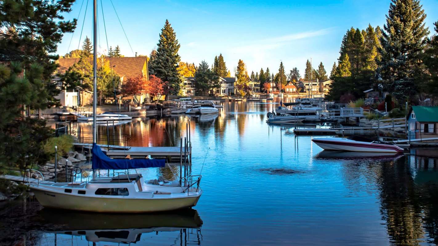 A tranquil marina scene with boats moored along a reflective waterway, surrounded by autumn-colored trees.