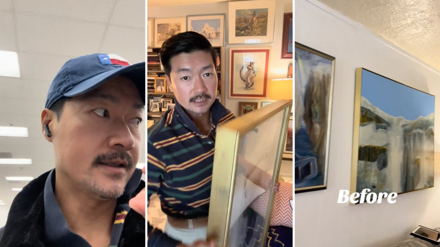 A man wearing a cap is holding a framed picture, surrounded by art and photographs.
