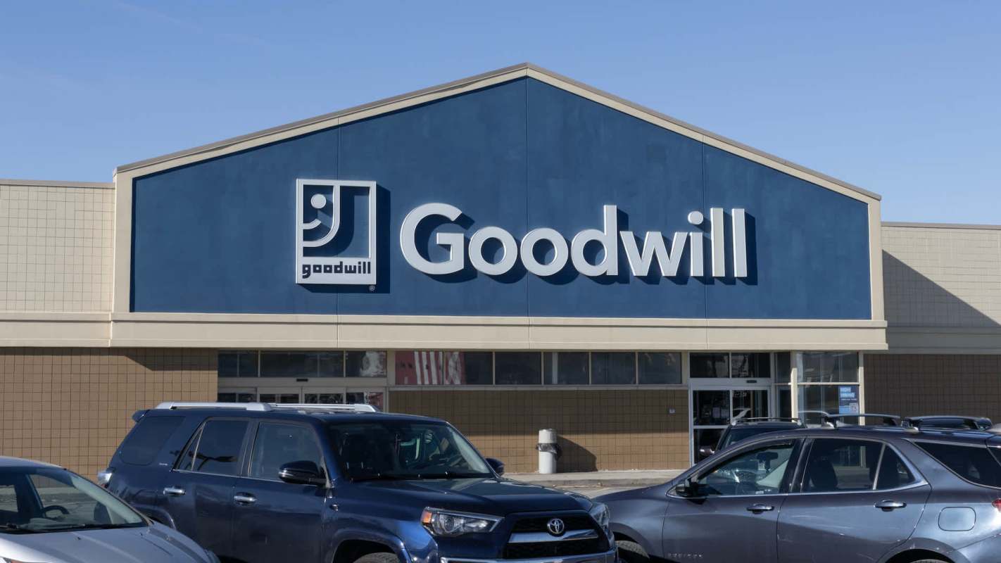 A Goodwill store front with a blue exterior and the logo prominently displayed, surrounded by parked cars.