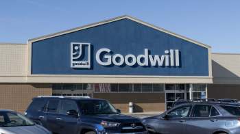 A Goodwill store front with a blue exterior and the logo prominently displayed, surrounded by parked cars.