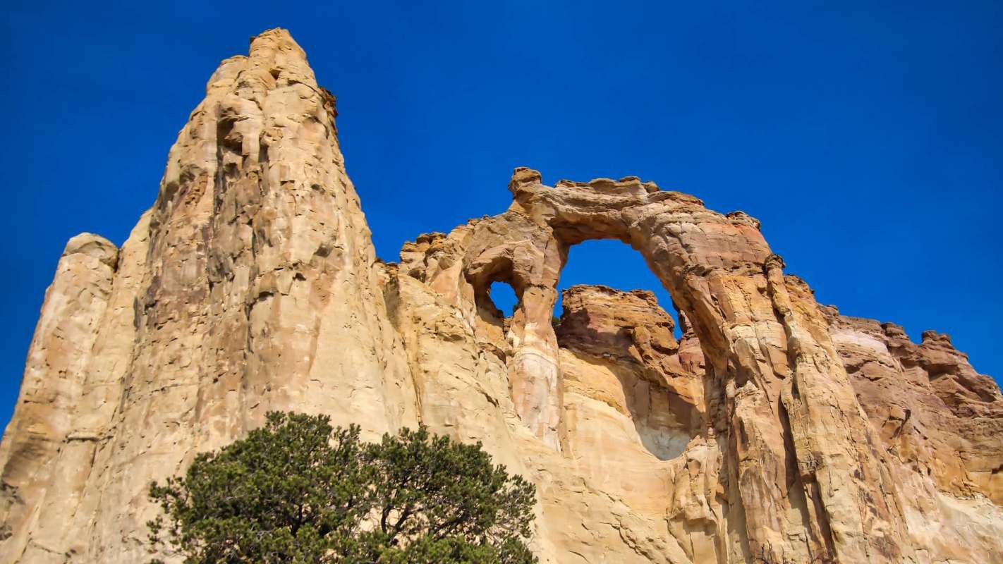A towering rock formation with an arch and hole, set against a clear blue sky.