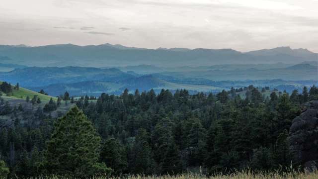 A panoramic view of rolling green hills and layered mountains under a cloudy sky at dusk.