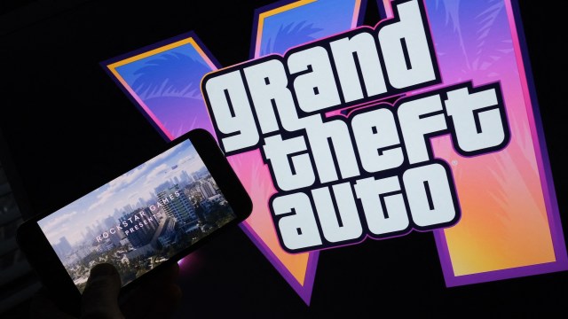 A game trailer playing on a smartphone in front of a Grand Theft Auto logo.