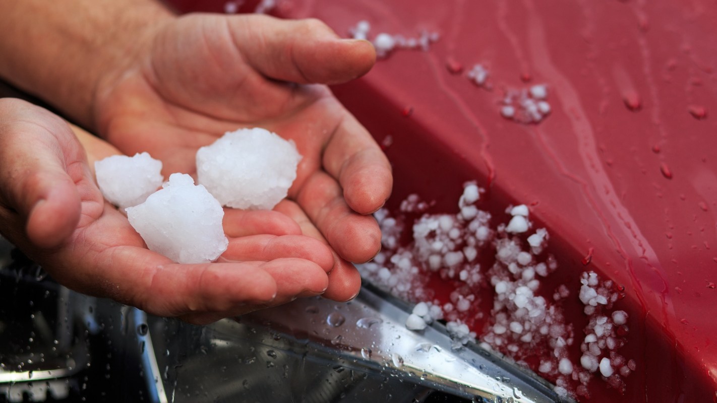 A person's hands hold large hailstones, with smaller pieces scattered on a wet red surface nearby.