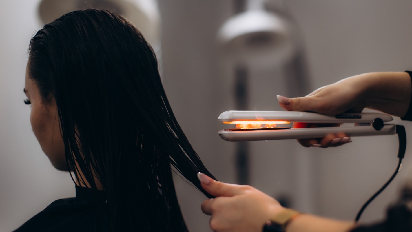 A hair stylist uses a flat iron on a client's wet hair.