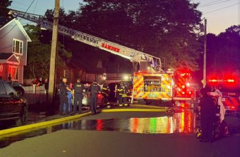 Emergency responders at night assist at a house fire scene with fire trucks and police present.