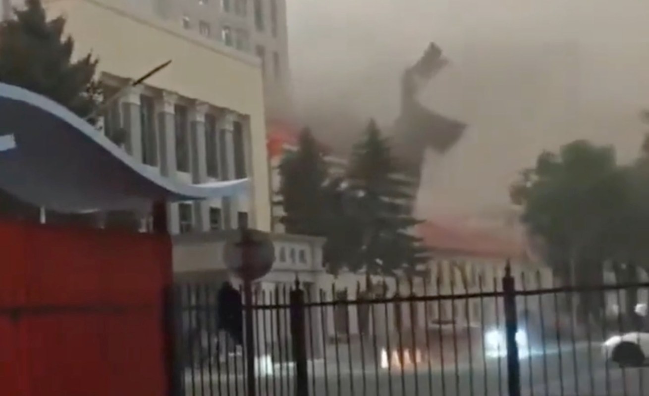A large piece of debris flies through the air near a building during a storm, obscuring visibility.