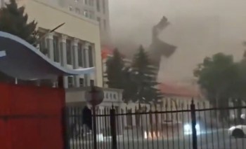 A large piece of debris flies through the air near a building during a storm, obscuring visibility.
