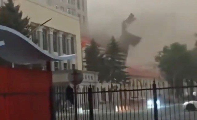 A large piece of debris flies through the air near a building during a storm, obscuring visibility.