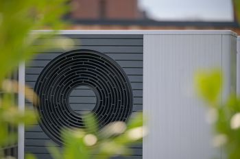 A heat pump unit partially obscured by greenery.