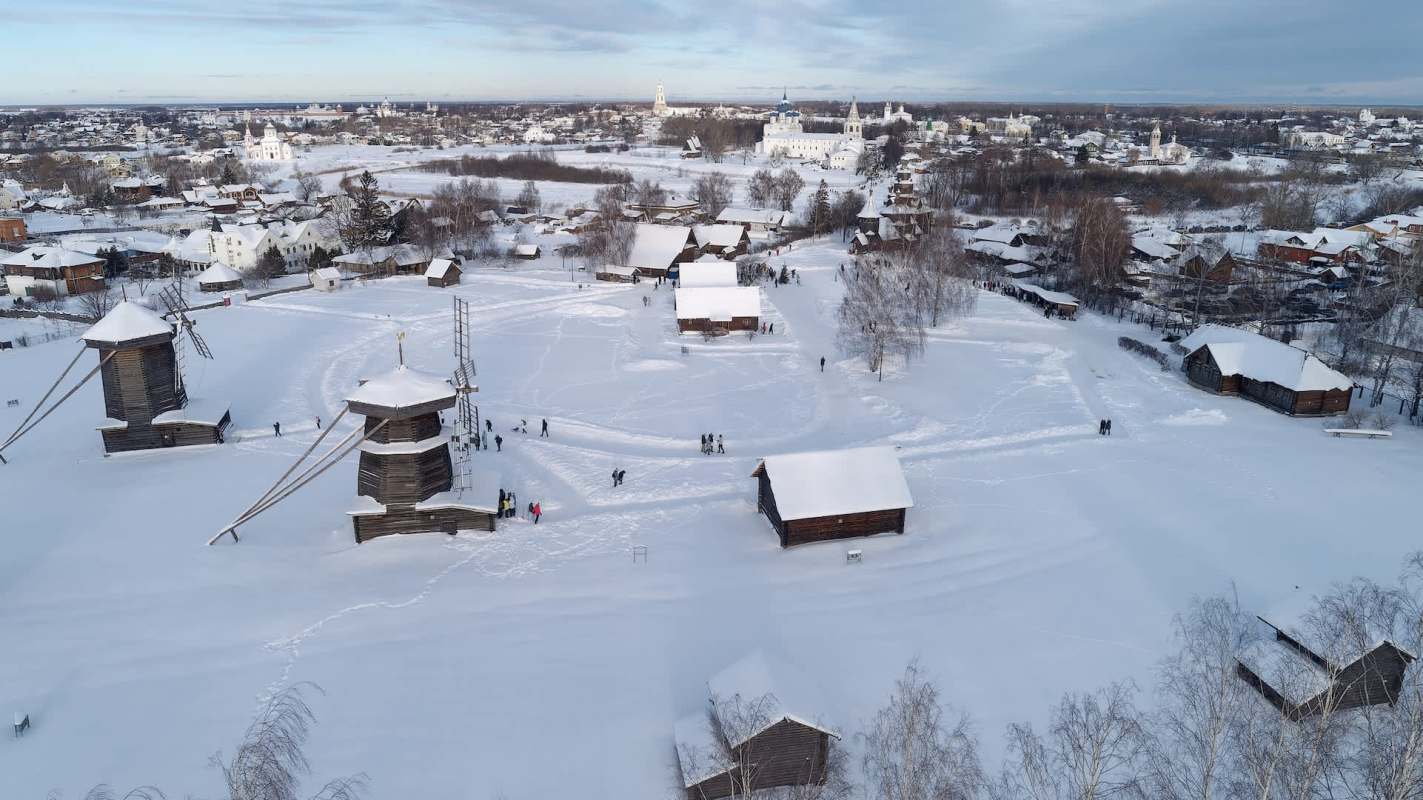 A snowy landscape featuring traditional wooden buildings and people walking in a historic village setting.